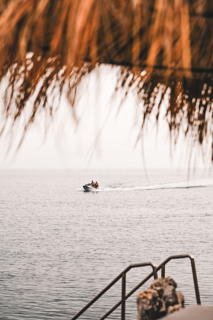 services-02 A jet ski glides across the ocean under a thatched roof with stairs leading into the water.