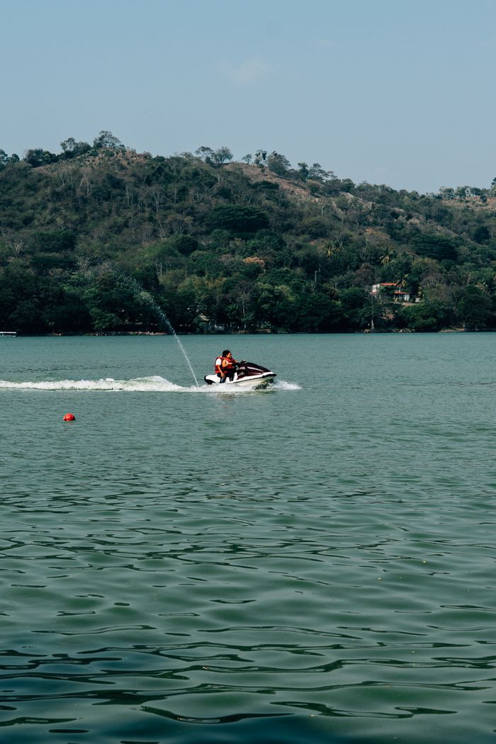 services-01 Couple enjoying a thrilling jet ski ride on a serene lake surrounded by lush hills.