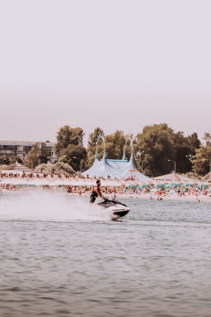 Person enjoying a thrilling jet ski ride on a crowded summer beach.